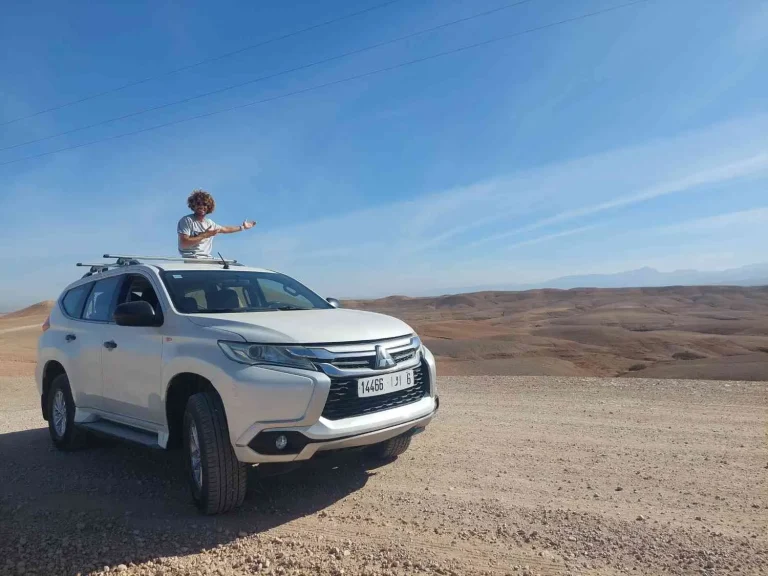 The founder of Poki Surf sits on the roof of the car and presents the view of the desolate rocky desert