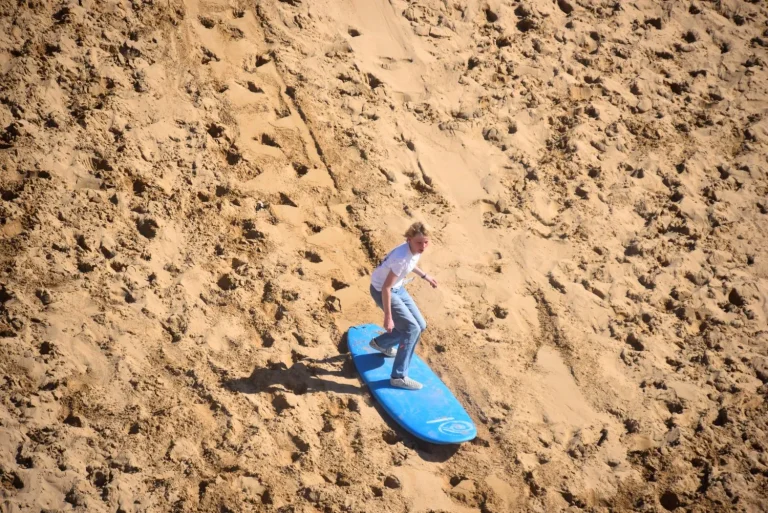 Child glides down the dunes on a surfboard