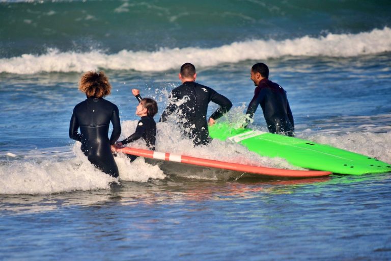 Two surf instructors accompany father and daughter on their way into the water, the little girl speaks with joy into the air