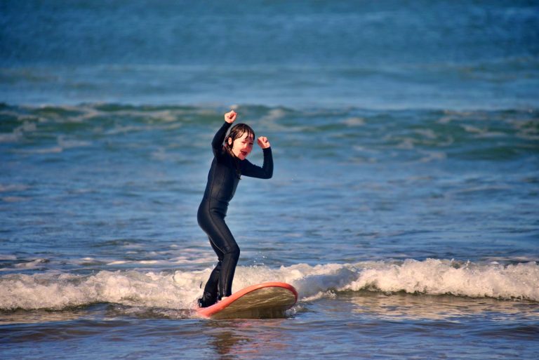 Little girl surfs a wave in the white water and stretches both arms in the air joyfully