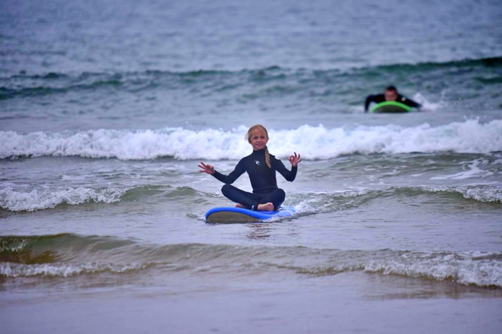 Little girl sitting in yoga pose on the surfboard and floating