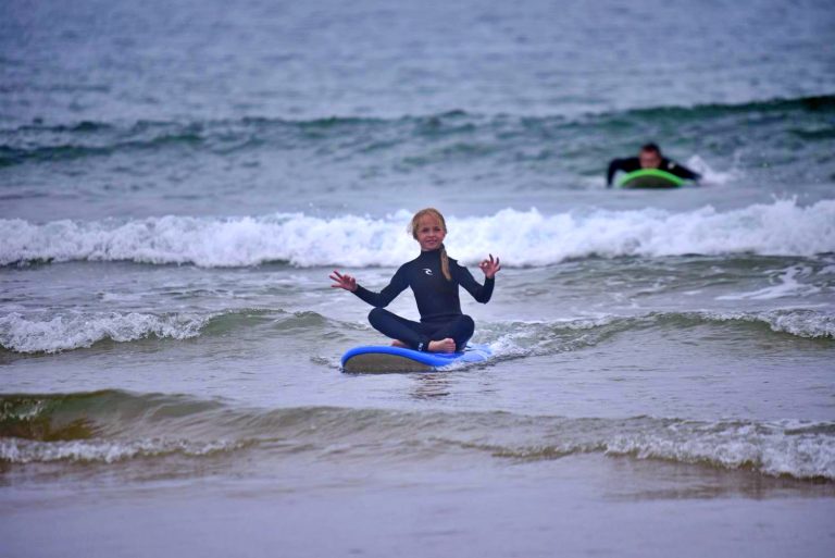 Little girl sitting in yoga pose on the surfboard and floating