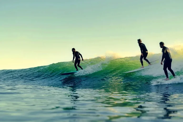 Three men ride a green wave together