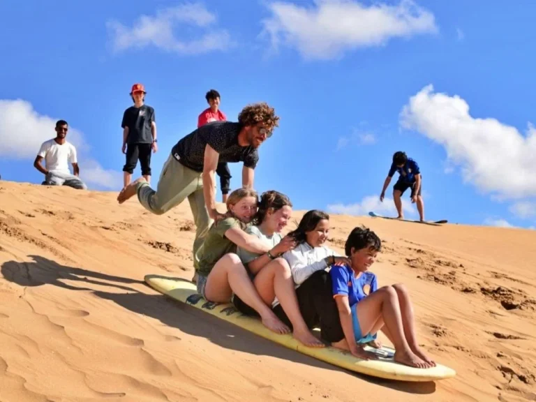 Kids surf together on a board down the dunes in the Little Sahara
