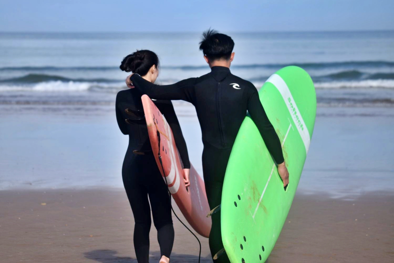 Young couple arm in arm on their way to surfing