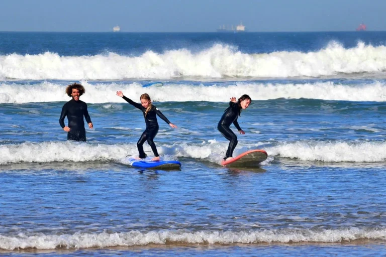 Two little girls, siblings, ride their first waves in the white water on the beach of Agadir