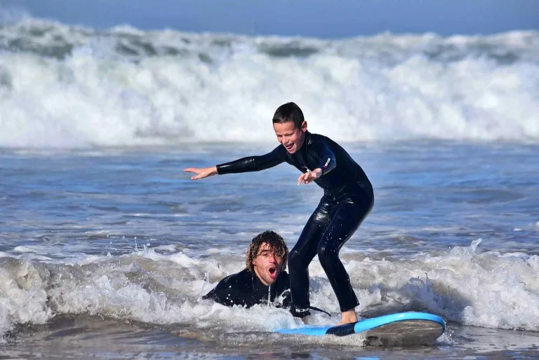 A little boy enthusiastically surfs his first wave while the surf instructor supports him