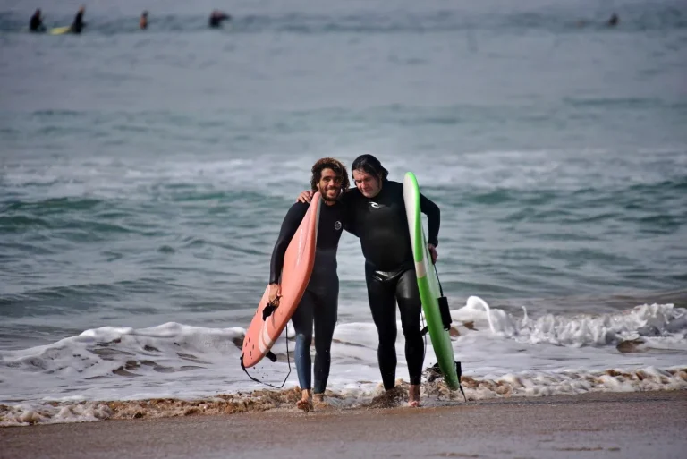 Surf instructor and course participants come out of the water arm in arm after a successful surf session