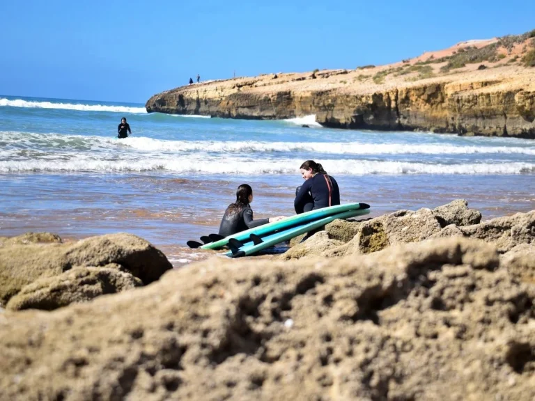 Participants in the surfing course sit on the rocks at the spot and watch the other surfers
